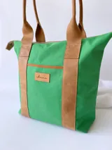Bolso tipo tote de lona color fucsia con asas de cuero marrón, bolsillo interno y externo.