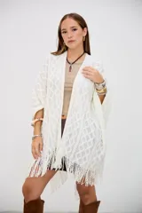 Poncho color crudo de tejido calado con diseño de rombos y flecos en el borde inferior.