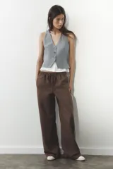 Chaleco gris con rayas verticales, escote en pico y cierre frontal con botones. Detalle de camisa blanca en el bajo.