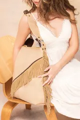 Bolso tipo tote de cuero color beige con textura natural y flecos de descarne color camel dispuestos en diagonal. Tiene correa de hombro ajustable con hebilla metálica.