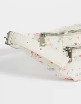 Riñonera color crema con estampado de flores pequeñas, correa ajustable con hebilla metálica, cierre superior y bolsillo frontal con cierre.