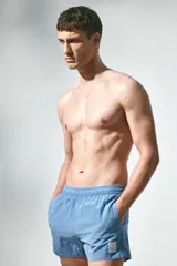 Short de baño azul de nylon con elástico revestido y cordón para ajustar oculto en la cintura, bolsillos laterales y bolsillo de solapa con cierre autoadherente atrás. Largo por encima de la rodilla con abertura corta en los laterales y suspensor interior en malla suave.