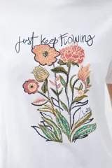 Remera blanca de algodón con cuello redondo y mangas cortas. Estampa frontal con bordado de flores y frase 'Just keep flowing'.
