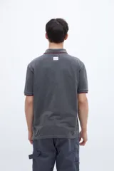 Chomba blanca de algodón con cuello clásico, media cartera de botones, bordado con la palabra 'Uniform' en el pecho y puños con rayas azul marino y rojo.