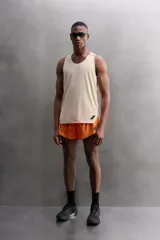 Camiseta deportiva sin mangas color beige, confeccionada en tejido técnico ligero y elástico con estructura perforada. Tiene cuello redondo amplio, sisas con acabados termofijados, bajo con aberturas laterales y logo estampado.