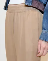 Babucha sastrera color beige confeccionada en tela italiana, de tiro medio y largo hasta los tobillos. Diseñada con cintura elastizada, cartera falsa, bolsillos laterales funcionales y piernas tipo pitillo con raya de aplomo.