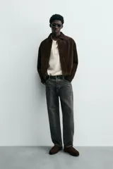 Cazadora de hombre de corte relajado confeccionada en piel con acabado ante, color marrón oscuro. Presenta cuello solapa, manga larga con puños abotonados a presión, bolsillos de vivo en cadera, bolsillo interior y bajo con elástico. Cierre frontal oculto por solapa con botones a presión.