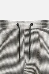 Short de baño con textura seersucker a rayas verticales azul marino y blanco. Tiene cintura elástica ajustable con cordón, bolsillos frontales y traseros, aberturas laterales en el bajo y forro interior.