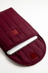Funda acolchada para laptop color bordó, con diseño capitoneado de líneas verticales y solapa curva con cierre.