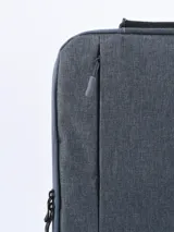 Mochila gris con múltiples bolsillos con cierre y asa superior. Ideal para transportar una laptop y otros objetos personales.