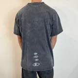 Remera negra con efecto lavado y estampado rectangular con imagen de surfistas en la playa y texto "Visions" en color lila. Corte oversize.