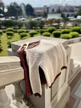 Sweater de punto calado color crema, con cuello, puños y ruedo en marrón con lurex. El cuello puede usarse de dos formas: mostrando un hombro o de forma clásica.