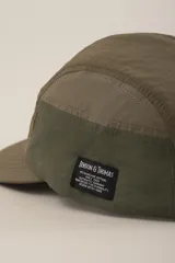 Gorro tipo cap verde con paneles de diferentes texturas y etiqueta con logo en el lateral.