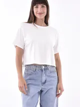 Remera corta color blanco hueso, de corte holgado y mangas cortas. Presenta cuello redondo y ruedo con flecos de strass. 