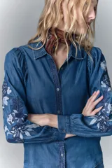 Camisa de calce recto confeccionada en tencel azul denim, con manga larga amplia con frunces en los hombros y cuello camisero. Presenta bordado de hilo en mangas y cartera. Mangas terminadas en puño con botón y ojal. Cartera delantera con botones metálicos con el logo de la marca.