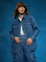 Sobrecamisa de denim azul con cuello camisero, cierre frontal con botones a presión, mangas largas con puños abotonados, dos bolsillos con solapa abotonada en el pecho y corte recto.