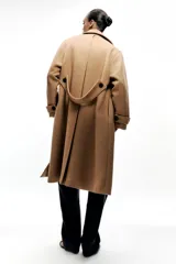 Abrigo color camel confeccionado en hilatura con lana. Tiene cuello solapa, manga larga, bolsillos delanteros ocultos en costura y cierre frontal cruzado con botones negros.