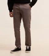 Pantalón de vestir marrón, de corte skinny, con bolsillos laterales y traseros. Se ajusta a la cintura con cinturón de cuero marrón.