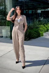 Blazer corto color beige, de manga corta, con solapas y cierre frontal con un botón. Presenta bolsillos de parche en la parte delantera.