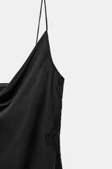 Vestido lencero de satén negro, corte midi asimétrico, con escote fluido y tirantes finos. Presenta drapeado lateral y aplicación de encaje a tono en el bajo.