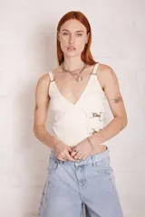 Top blanco de jersey de canalé, con escote en V envolvente, tirantes anchos y detalle de herrajes metálicos con hebilla funcional en el lateral.