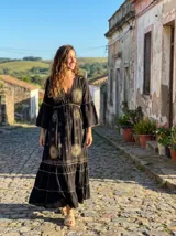 Vestido largo negro con bordados dorados de soles y estrellas, escote en V con cordones, mangas acampanadas y falda con volados.