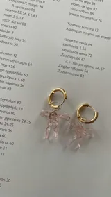 Par de aros colgantes con argollas de acero inoxidable y dijes de vidrio soplado con forma de moño, disponibles en color celeste y rosa.