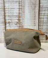 Neceser de lona color verde oliva con detalles en cuero color marrón. Tiene cierre superior y un parche de cuero con el logo de la marca en el frente.