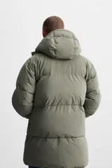 Cazadora acolchada negra de tejido técnico, cuello alto con capucha ajustable, manga larga con puño interior elástico, bolsillos laterales y bolsillo interior. Cierre frontal con cremallera oculta y botones a presión.