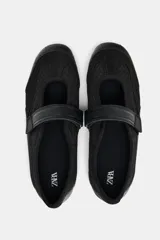 Zapato tipo bailarina color negro, con capellada de rejilla y ajuste con tira de velcro.
