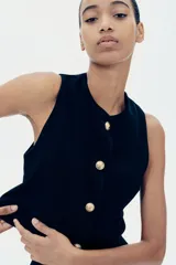 Chaleco cropped negro en punto bouclé con cuello redondo, pinzas en el busto, botones a presión dorados y forro interno.