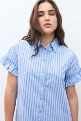 Vestido camisero corto color celeste con rayas blancas y finas rayas rojas. Presenta cuello camisero, botones frontales, mangas cortas con volados y un volado en el ruedo.