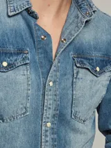 Camisa de jean celeste de manga larga con dos bolsillos frontales con solapa y botones nacarados.