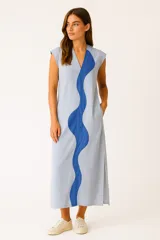 Vestido midi celeste con una franja azul ondulada en el frente, cuello en V y mangas cortas. Tiene bolsillos laterales y corte holgado.
