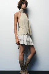 Falda pantalón negra de tiro bajo con cintura drapeada y bajo acabado en volantes superpuestos. Presenta un lazo largo y fino que cae desde el lateral.