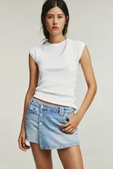 Falda pantalón corta de denim celeste, de tiro alto con cinco bolsillos y cierre frontal cruzado con botones metálicos.