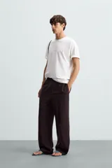 Camiseta blanca de corte holgado, cuello redondo y manga corta. Estampado frontal con texto en color negro y parche en la espalda. Detalle de pliegues en la espalda.