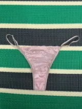 Bombacha tanga de encaje floral rosa pastel con tiras finas color beige y reguladores metálicos a los costados.