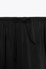 Pantalón negro de tejido fluido, tiro medio con cintura elástica ajustable con cordones, bolsillos laterales y falsos bolsillos de vivo en la espalda.