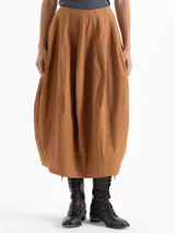 Pollera larga tipo balloon color marrón, confeccionada en popelina asargada. Presenta recortes verticales que aportan volumen y estructura, bolsillos ocultos en los laterales y bordado de logo JCH en el frente.