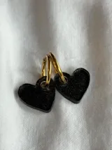 Aros colgantes con forma de corazón color negro y aro dorado.