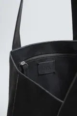 Bolso tipo shopper fabricado en piel con acabado serraje color gris oscuro. Tiene compartimento principal abierto con un bolsillo interior con cierre. Cuenta con dos asas de mano fabricadas en piel.