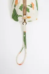 Neceser acolchado de nylon con estampado de cactus y flores en tonos verdes, naranjas y amarillos sobre fondo blanco. Posee asa de mano desmontable y herrajes metálicos dorados.