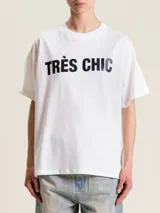 Remera blanca de algodón con cuello redondo y estampado negro con la frase "Très Chic" en el frente.