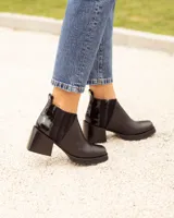 Botín Chelsea de cuero negro, con elástico lateral acanalado y detalle de cuero charol en el talón. Posee punta cuadrada y taco ancho y bajo.