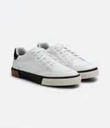 Championes urbanos blancos de cuero sintético con caña corta, recortes y suela tricolor texturizada.