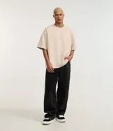 Remera oversized color beige confeccionada en gamuza sintética. Presenta cuello redondo, mangas cortas y bordado de cruz en el frente.
