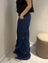 Pantalón cargo negro de denim rígido, corte wide leg, con bolsillos laterales y detalles de tiras con hebillas en los laterales.