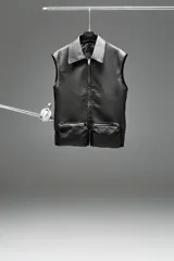 Chaleco negro de cuero sintético con cuello clásico, cierre frontal con cremallera y dos bolsillos tipo pouch con cremallera.