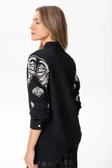 Camisa negra de lino con bordados florales blancos, de corte clásico, cuello camisero y mangas largas con puños abotonados.